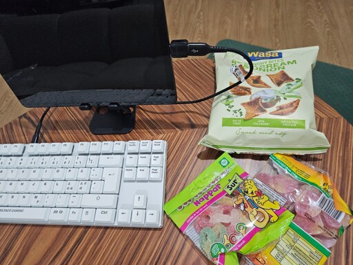 An image showing a physical keyboard attaches to a tablet with a USB-cable. Next to them to the right are one bag of rye potato chips and two bags of sour candy.