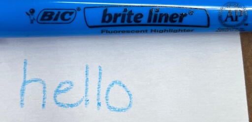 A blue BIC Brite Liner Highlighter above the word "hello" handwritten out on paper with that highlighter. The "hello" looks as if it was written with a crayon instead.